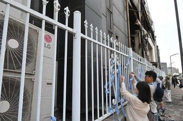 불에 탄 아리셀 공장 담장에 추모 리본을 달고 있는 참가자들.